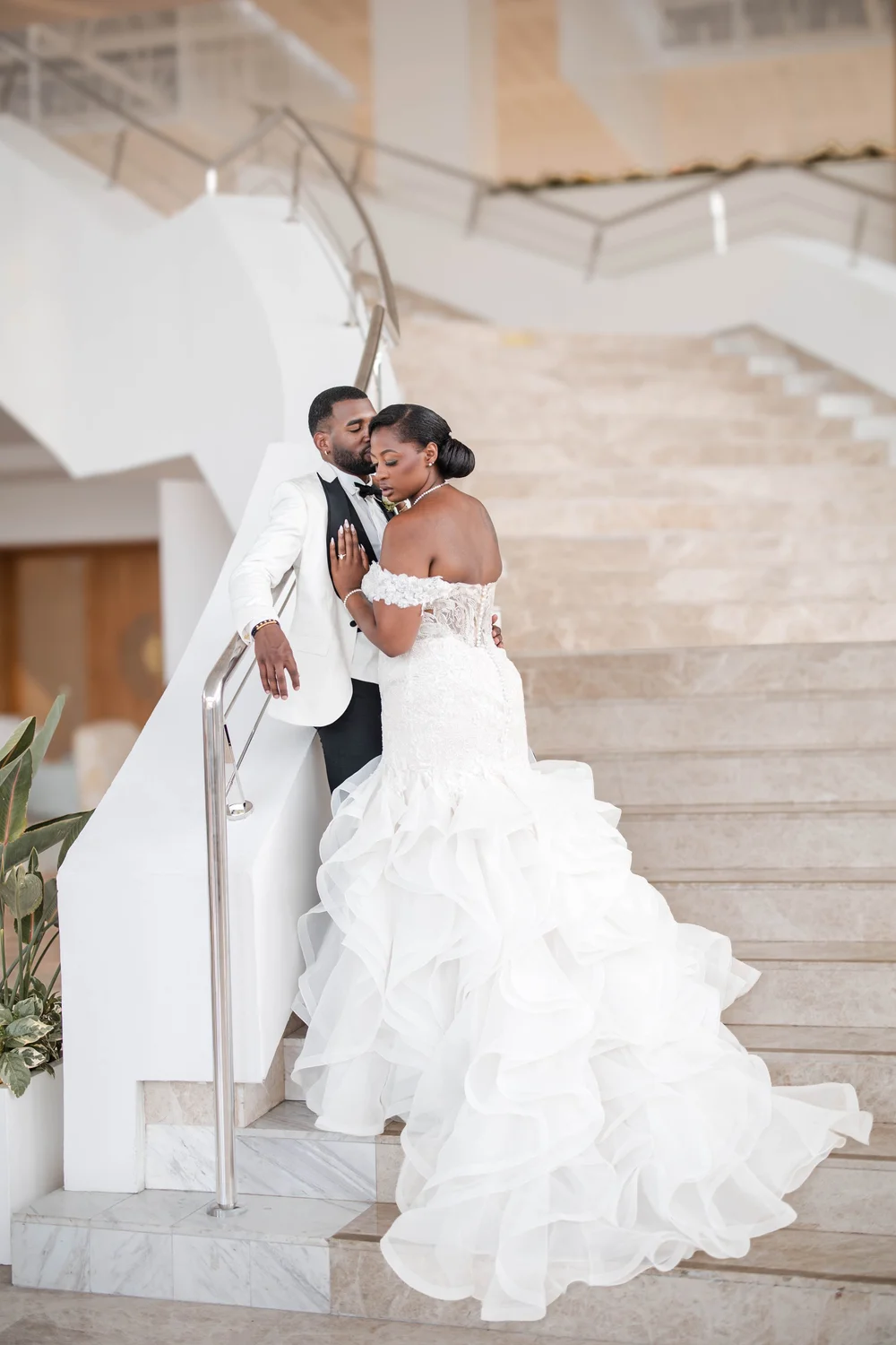 A couple on a curved white staircase, the bride's ruffled train spread behind her