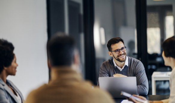 A man in glasses smiling at board members during a meeting