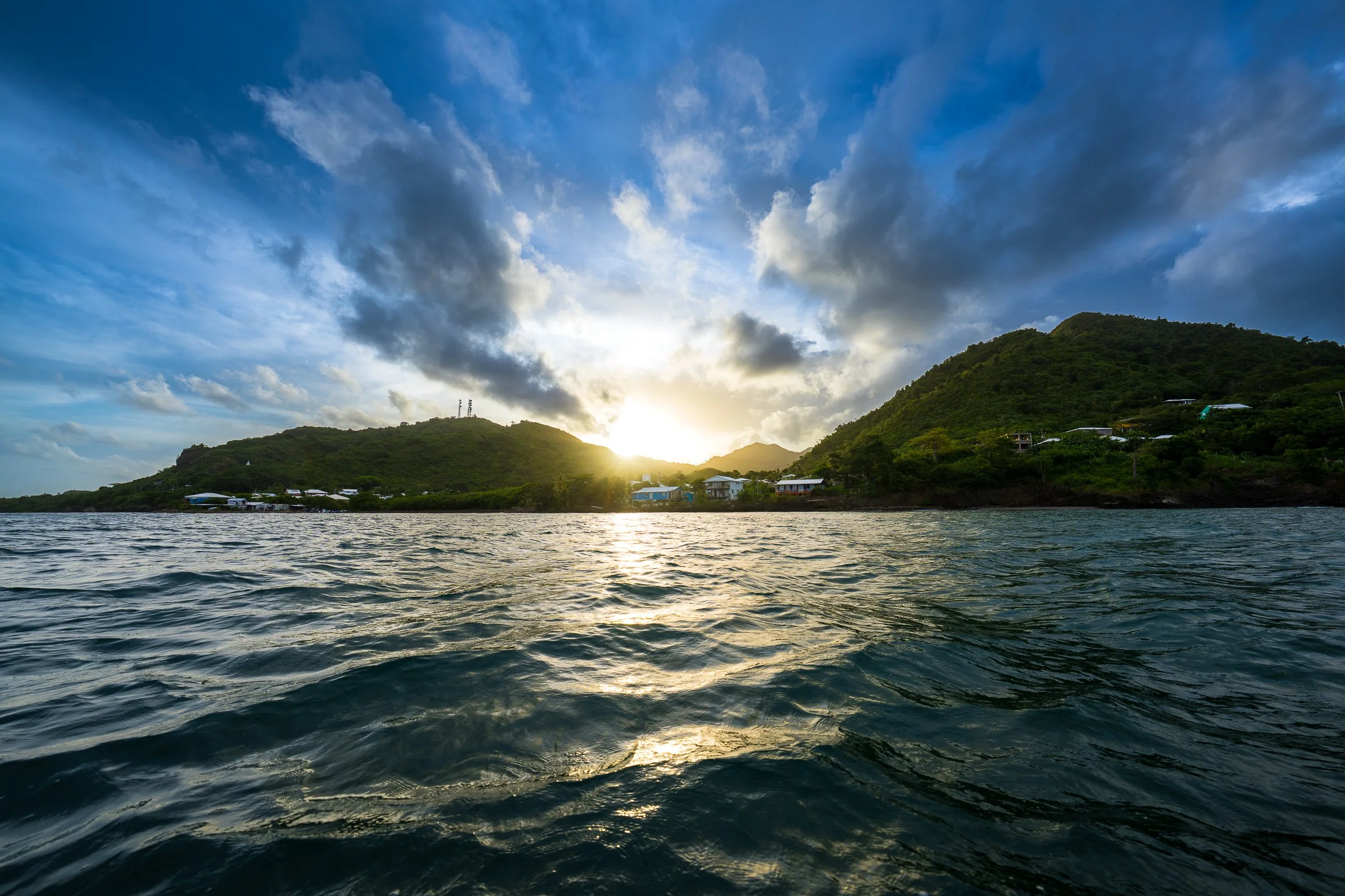 Soft sunset rays break between hills across a textured bay and deep blue clouds.