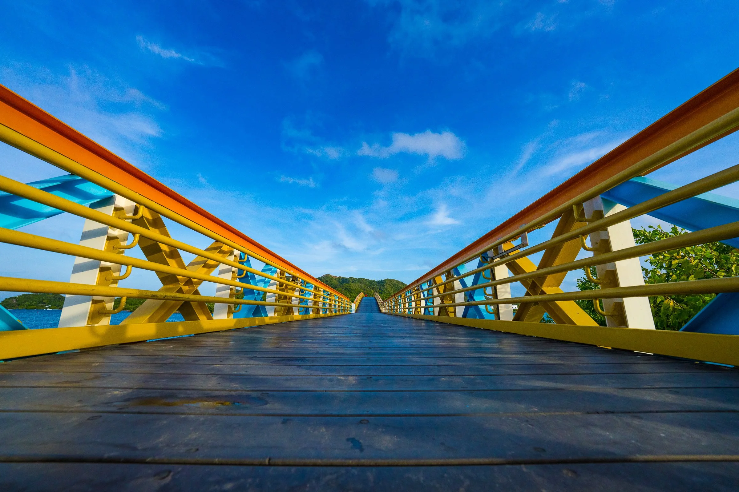 A low view along a colorful yellow bridge under a deeply saturated blue sky.