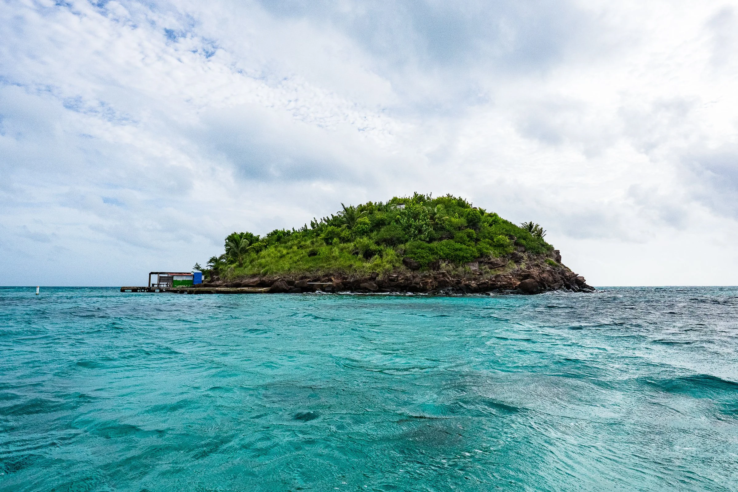 A small green island rises from aqua water beneath a softly overcast sky.