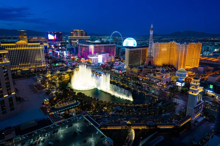 Bright white fountain jets illuminate the Bellagio lake beneath a deep blue night sky and glowing hotels.