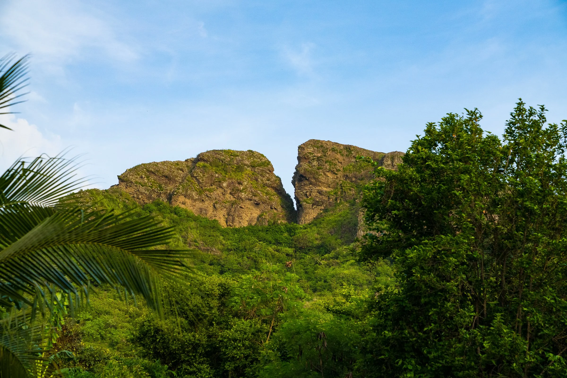 Two steep rocky green hills meet at a narrow gap above tropical forest.
