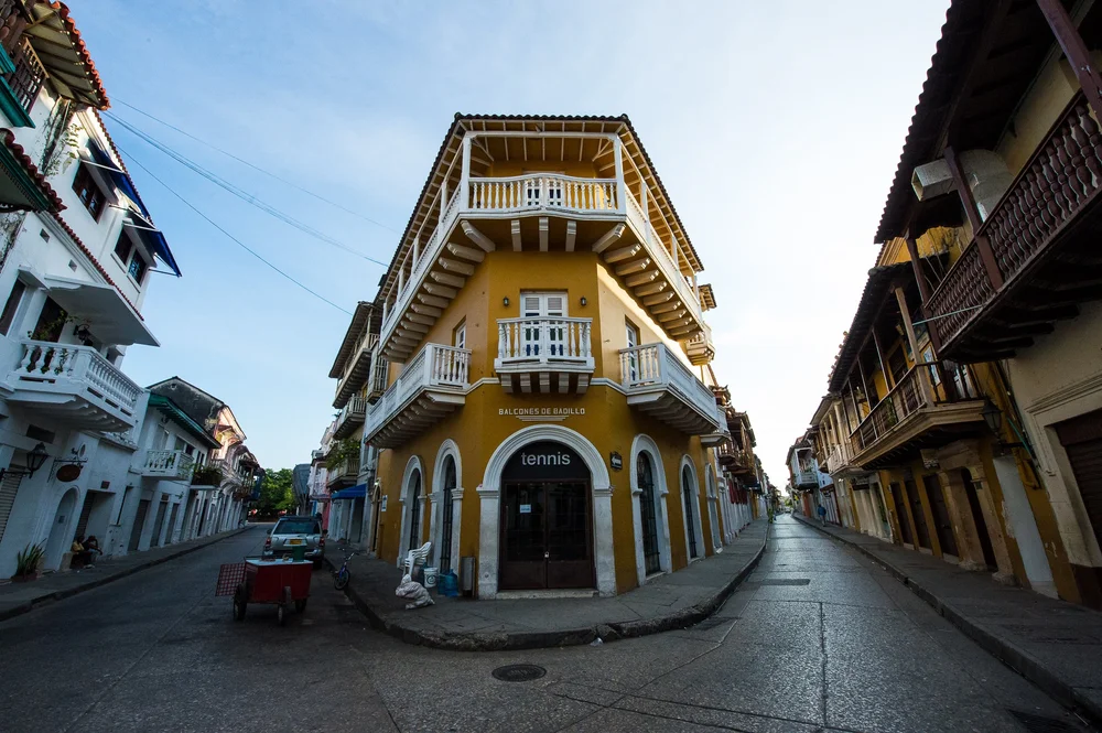 White-railed balconies rise above the rounded corner entrance of a warm-colored building.