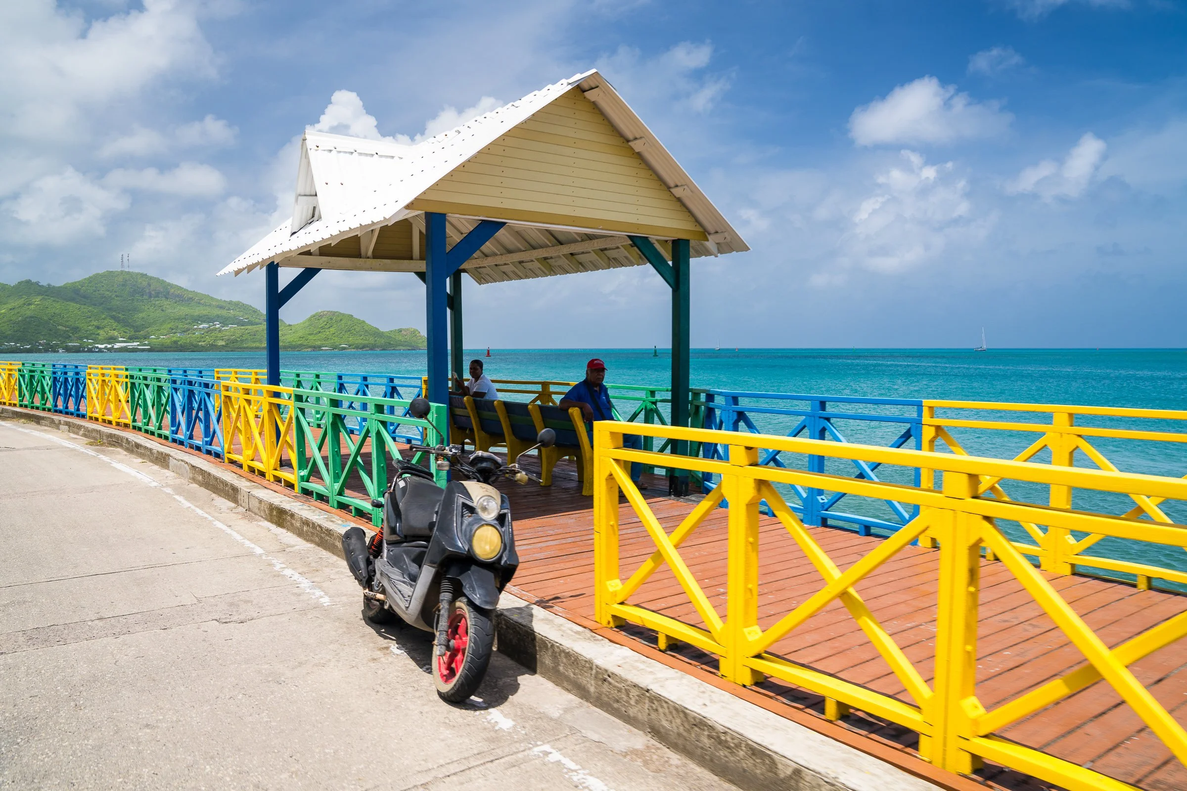 A brightly painted waterfront railing and shelter beside the turquoise Caribbean sea.