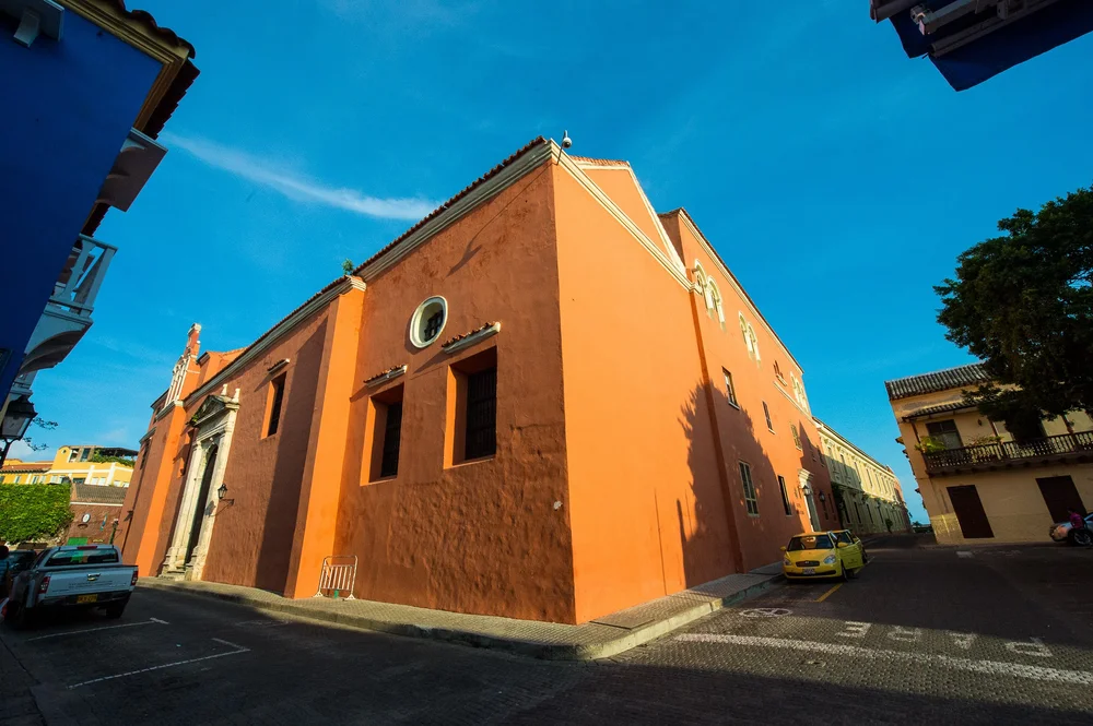 A terracotta-colored corner house meets a clear blue sky above a quiet stone street.