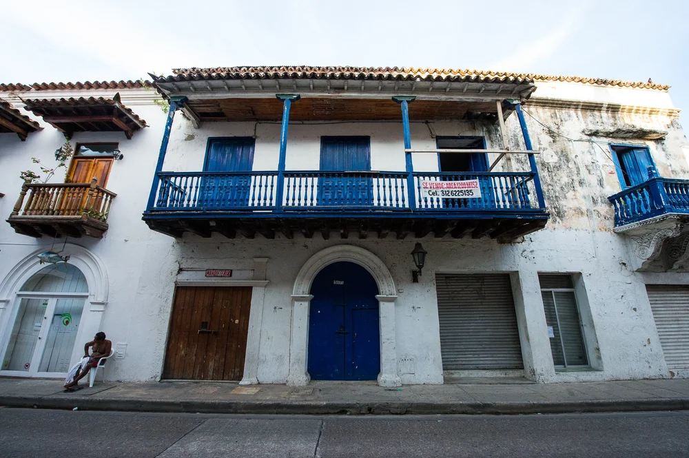 Blue doors and a long blue balcony punctuate an aged pale facade.