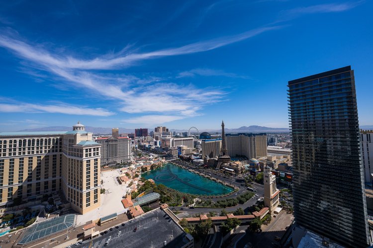 Sunlit Las Vegas hotels and a turquoise lake seen from above beneath a vivid blue sky.