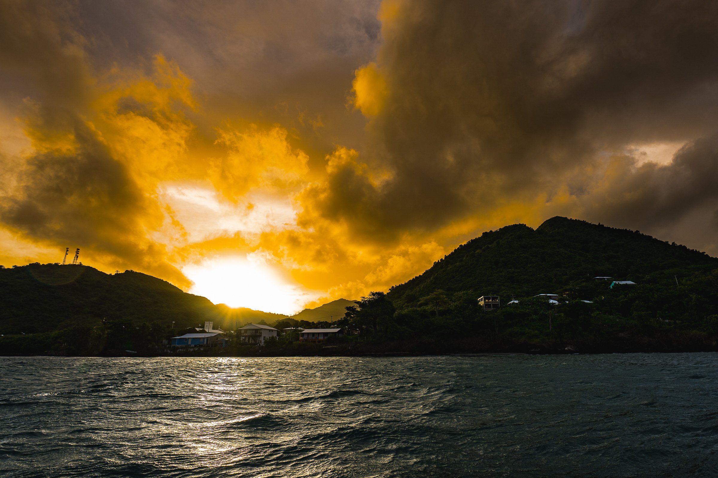 Dramatic gold-lit clouds rise behind a dark island ridge above rippling water.