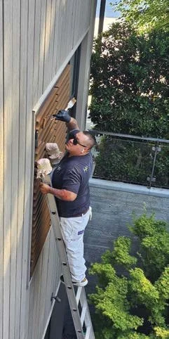 Painter restoring exterior siding from a ladder