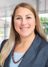 Clare is smiling in her headshot. She is wearing a light blue blouse, blue-gray suit jacket, and brown necklace.