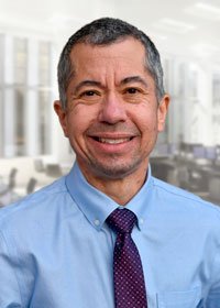 Sean is smiling in his headshot. He is wearing a light blue button-down shirt and a blue geometric tie.