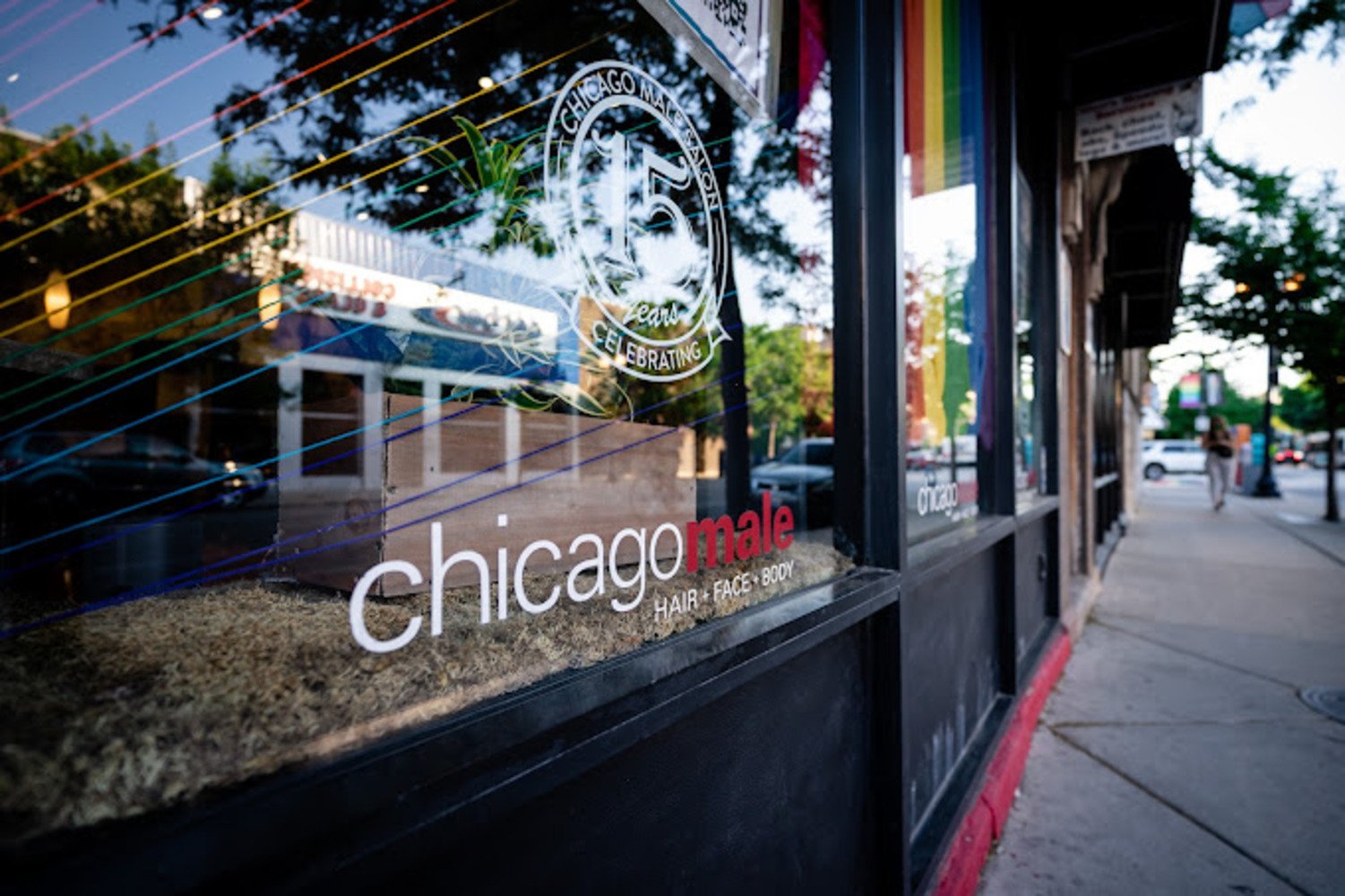Storefront window of Chicago Male Salon with a 15-year anniversary decal and street reflections.