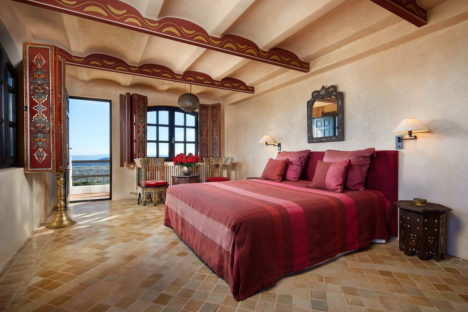 Dormitorio con cama roja, techo de vigas y acceso a la terraza.