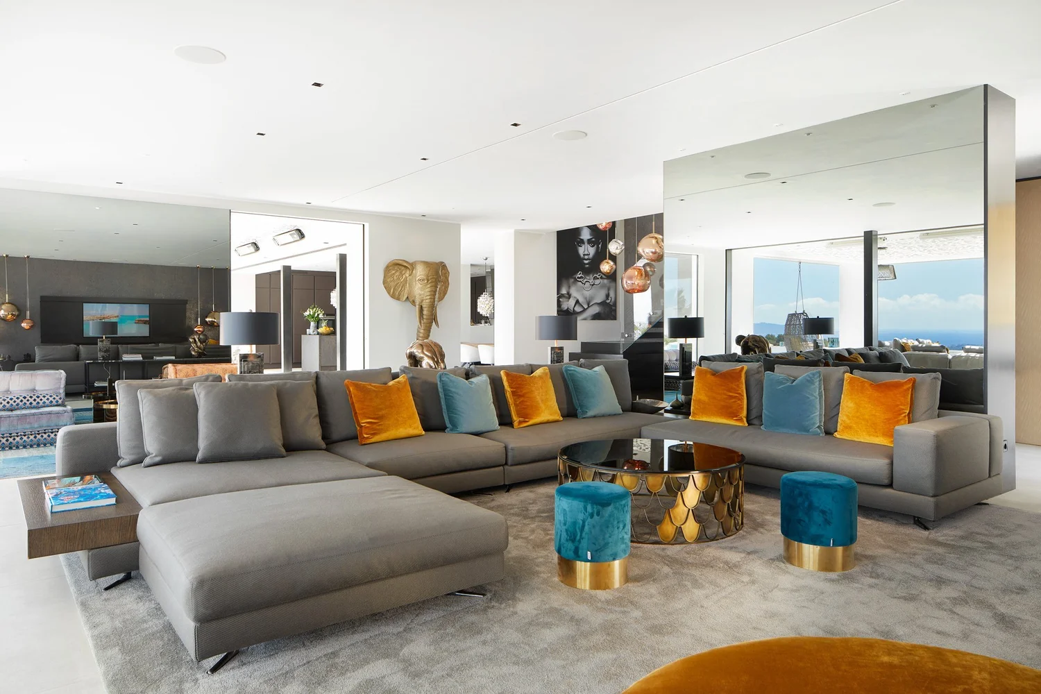 Sala de estar con sofás grises, cojines azules y amarillos y vistas al mar.