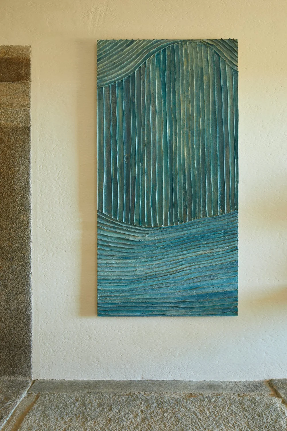 Obra abstracta azul y verde sobre una pared clara.