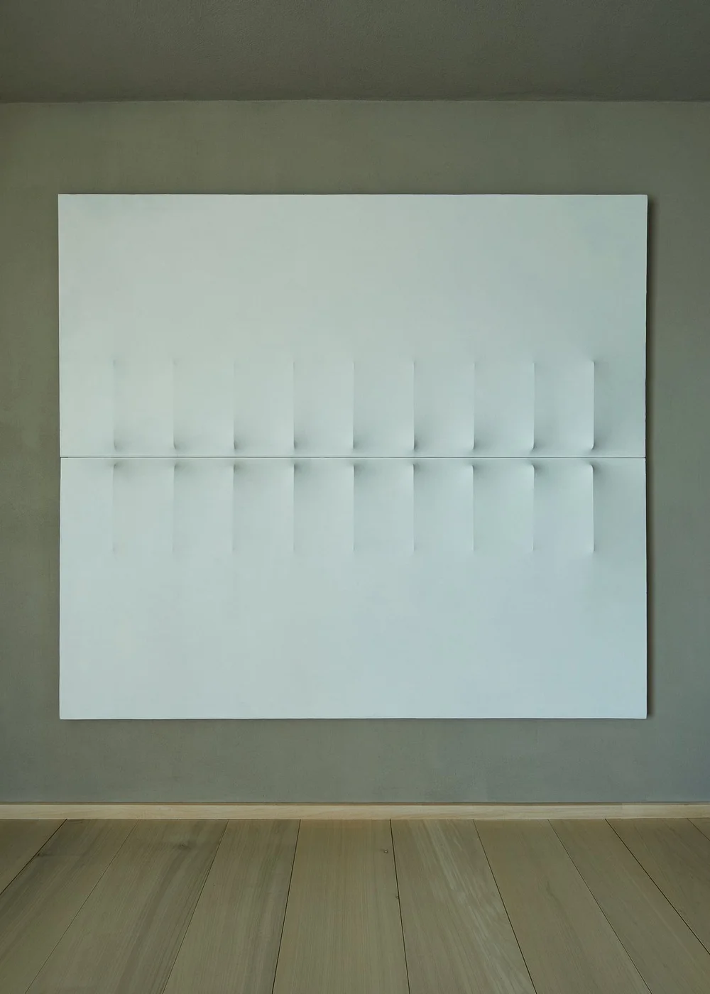 Obra blanca con relieve lineal en una pared de tonos neutros.