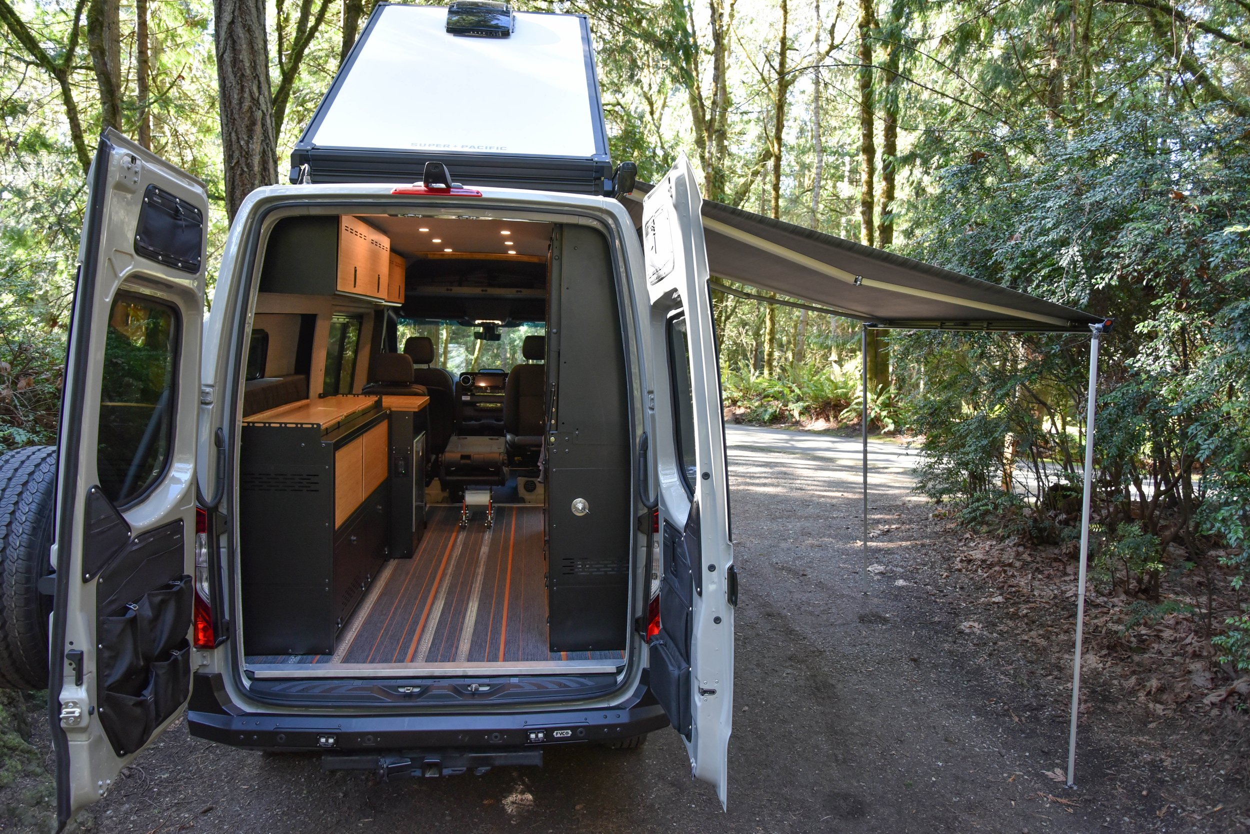 Camper van with rear doors open at a woodland campsite