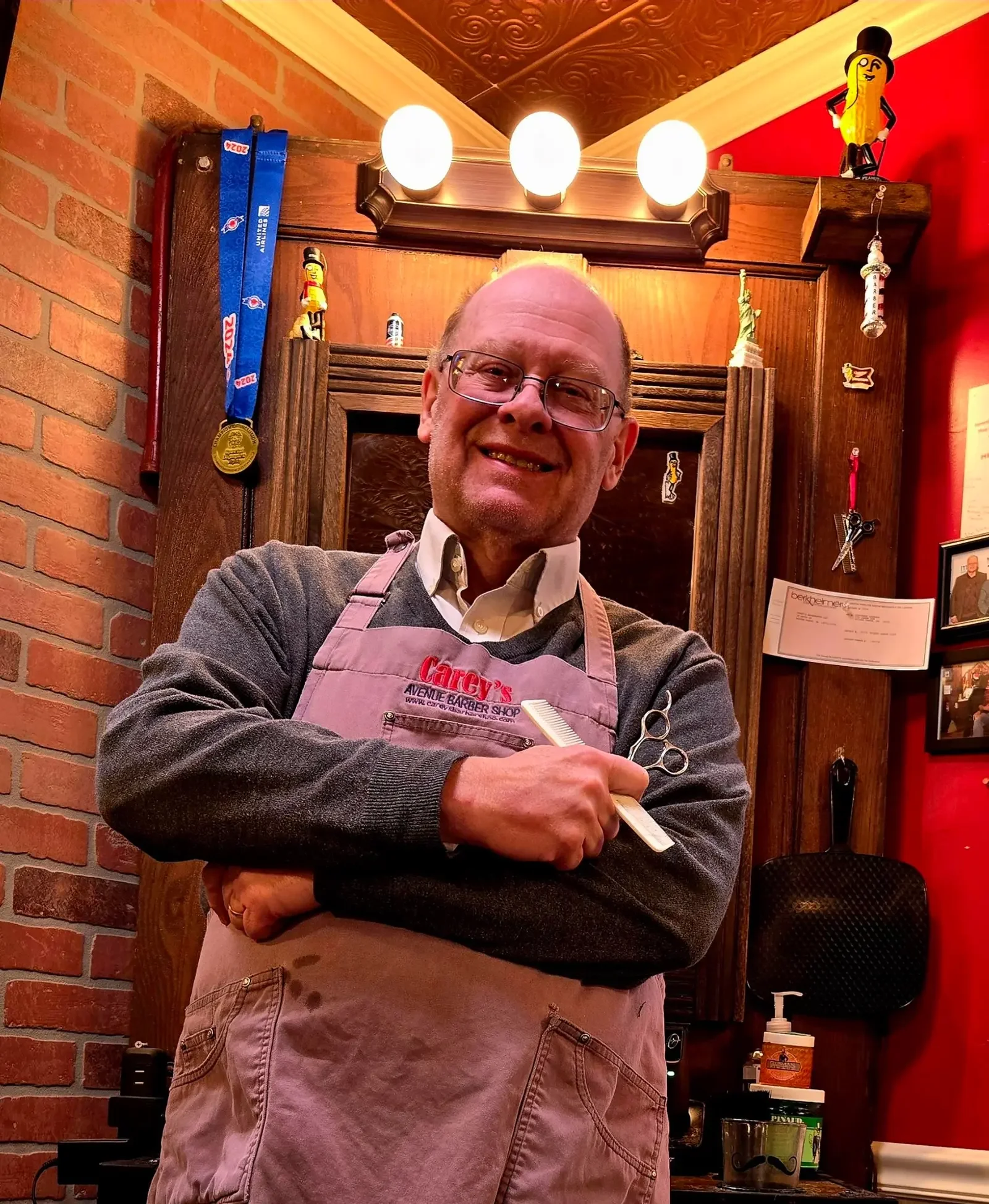 Dan Carey in his barber apron holding a comb and shears