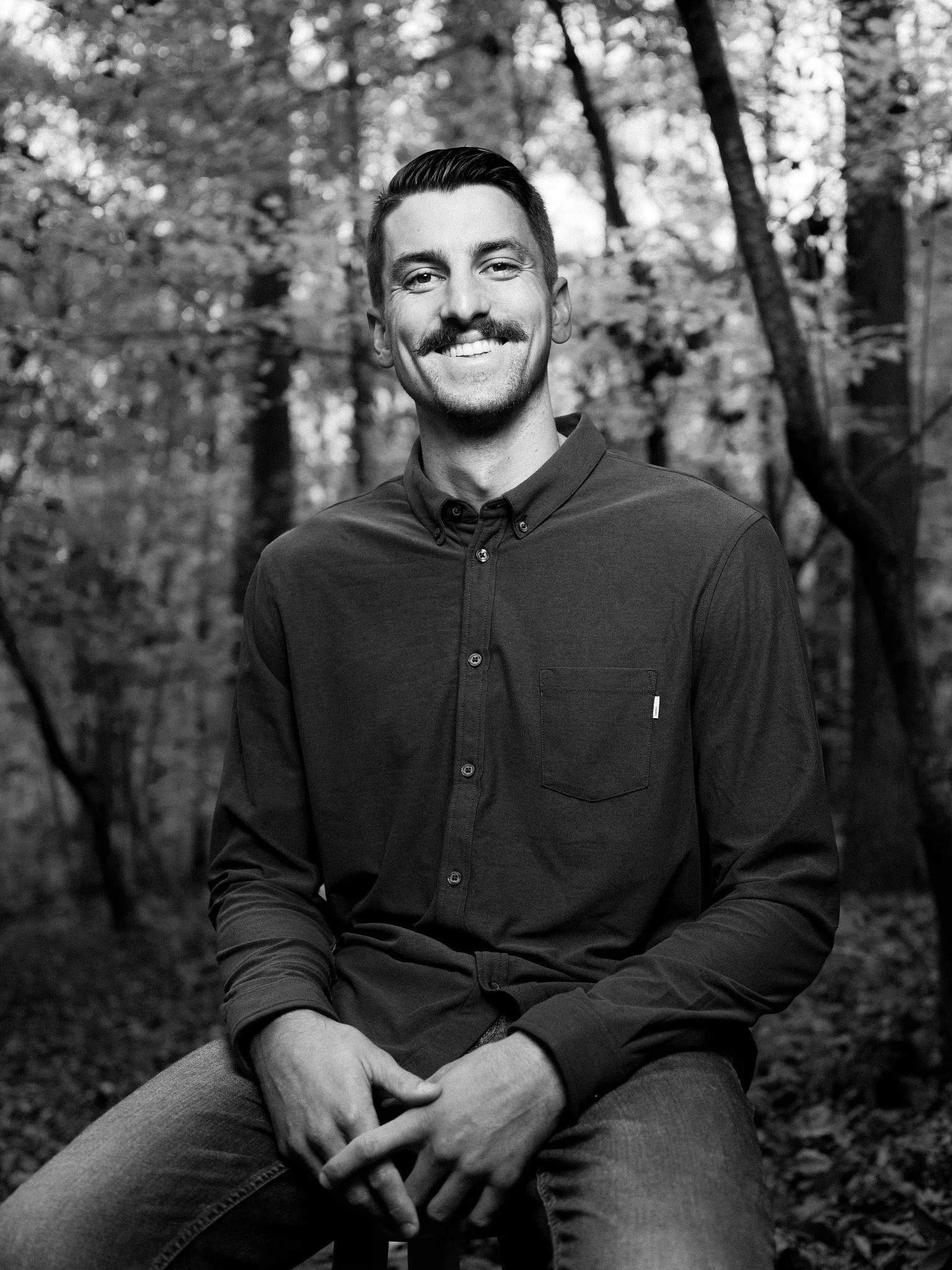 Bryce Ridenour smiling while seated outdoors among trees