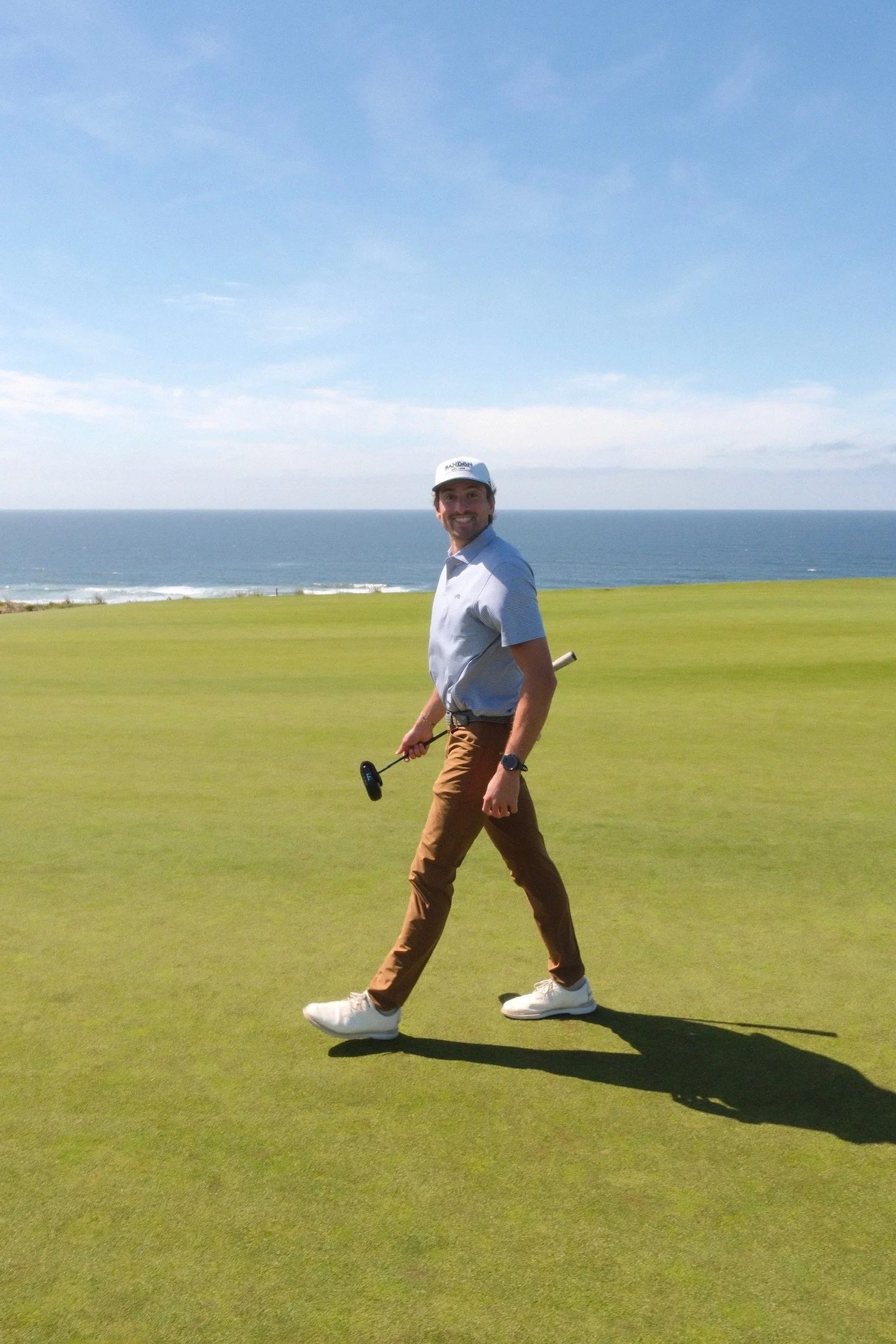 Bryce smiling while walking across a golf course beside the ocean
