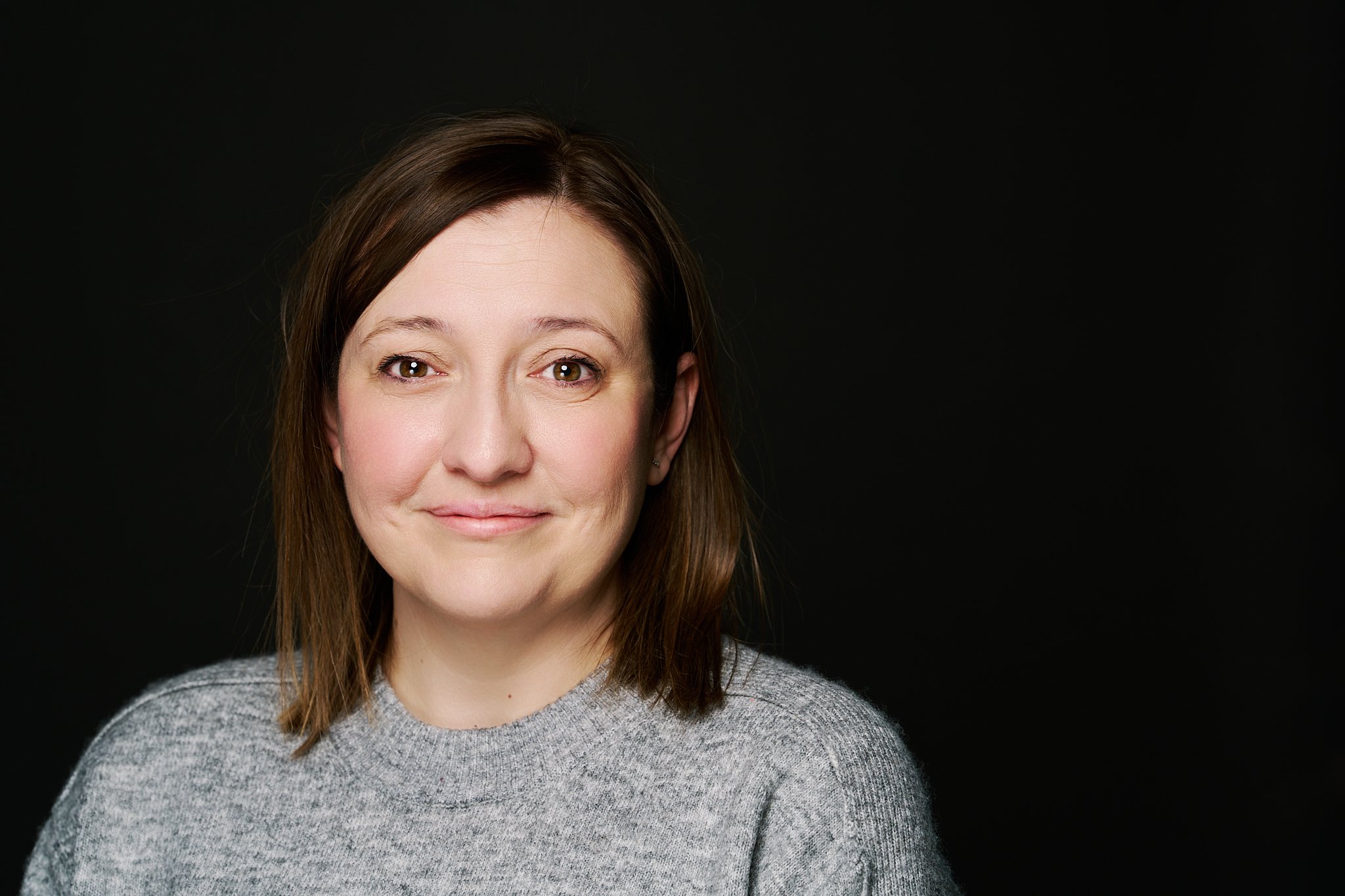 Professional female corporate headshot — warm, natural studio portrait on dark background