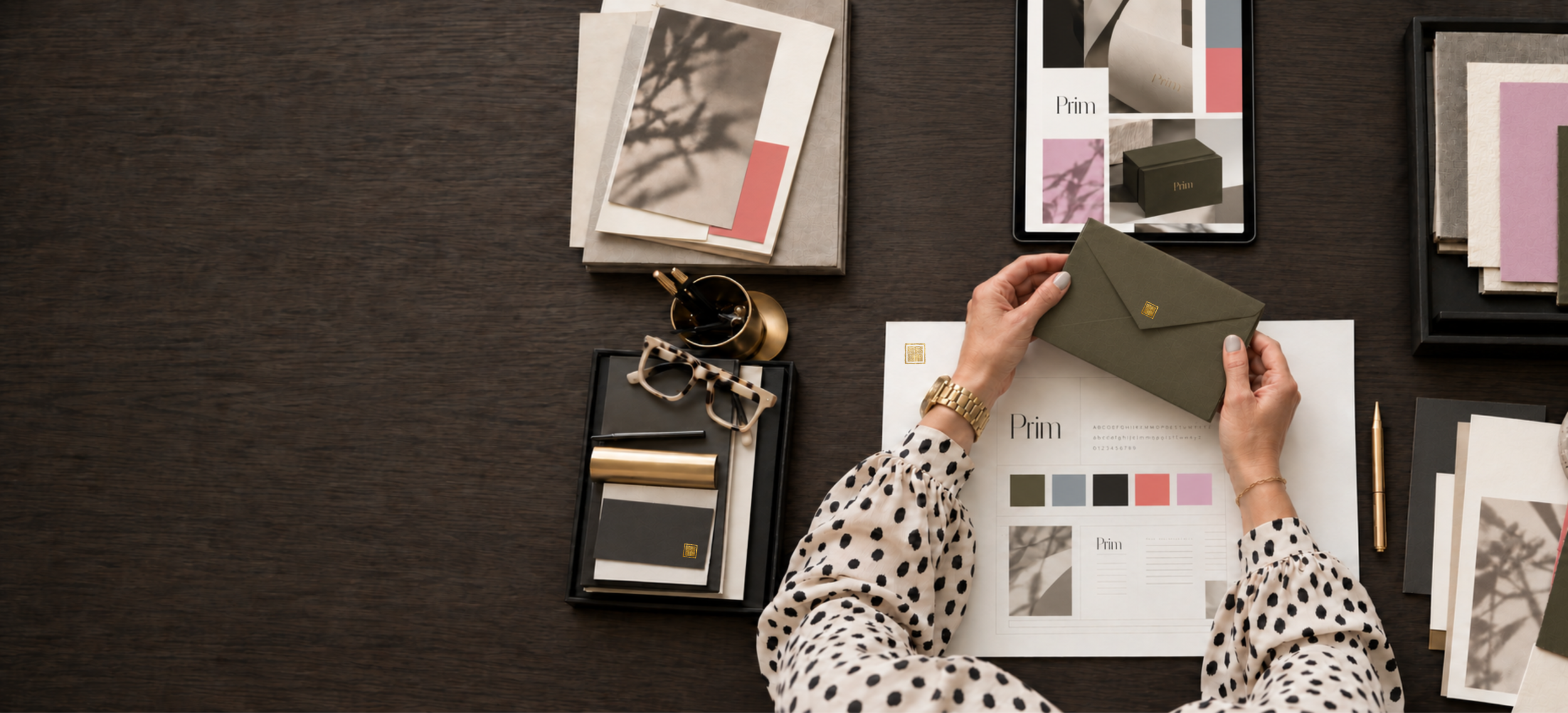 Prim brand materials on a walnut desk &mdash; colour swatches, typography sheet and a gold-sealed envelope