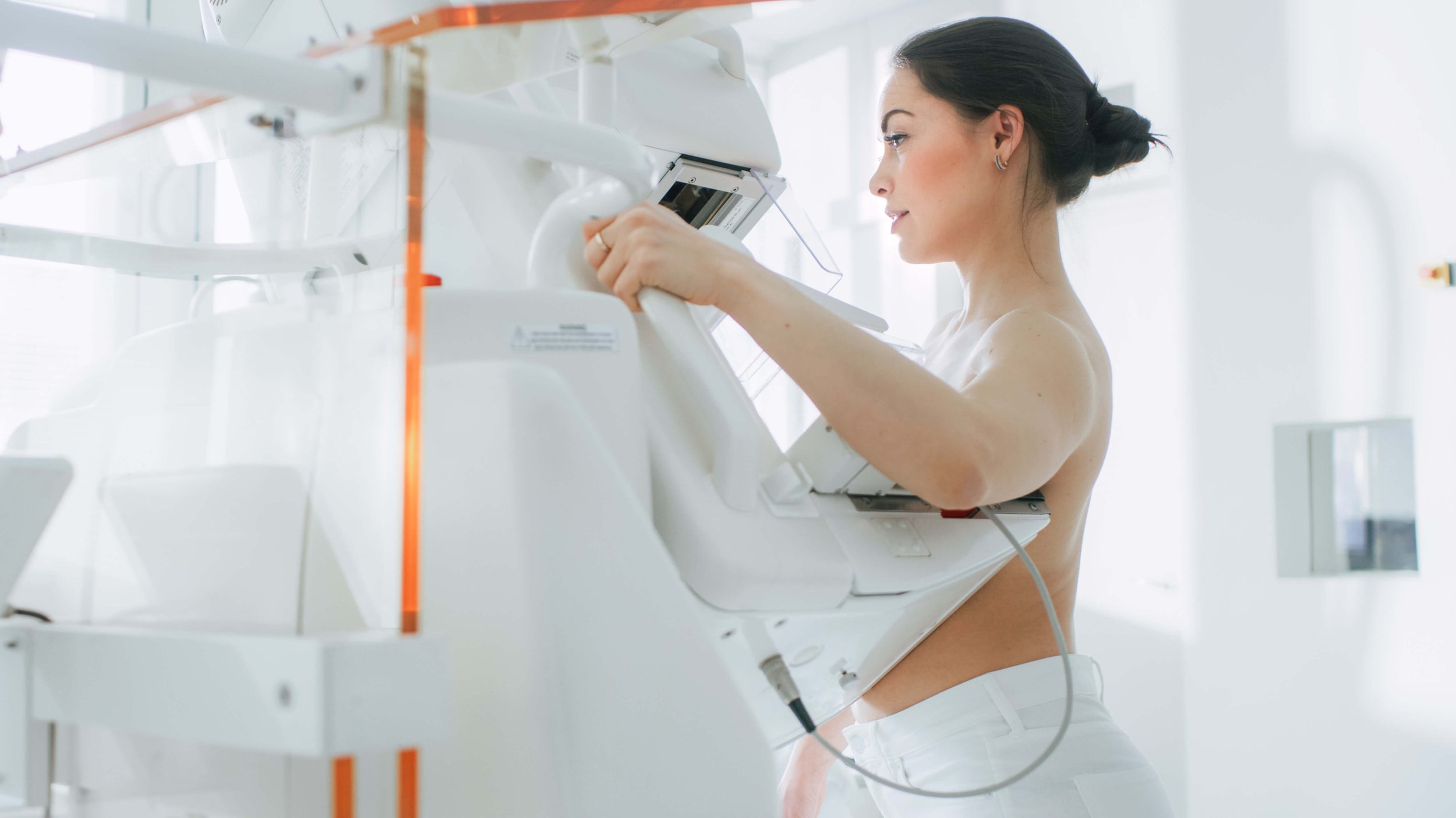 To show what to expect during a mammogram, a woman stands at a mammogram machine, getting her breast screening done.