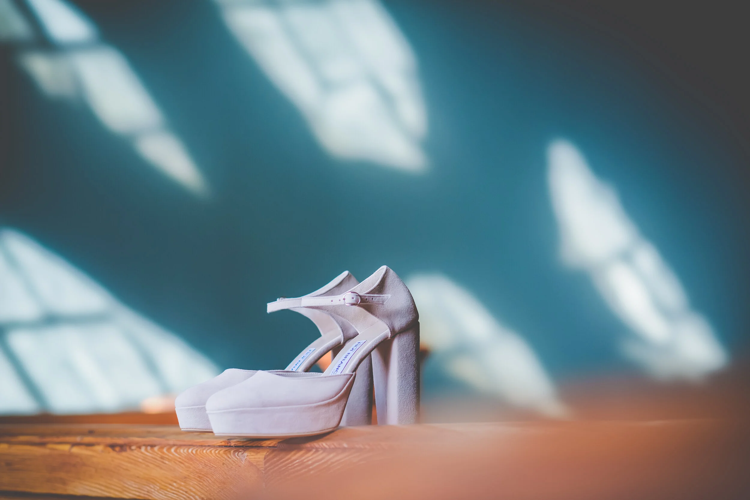 Bride’s wedding heels on a wooden table in soft sunlight.