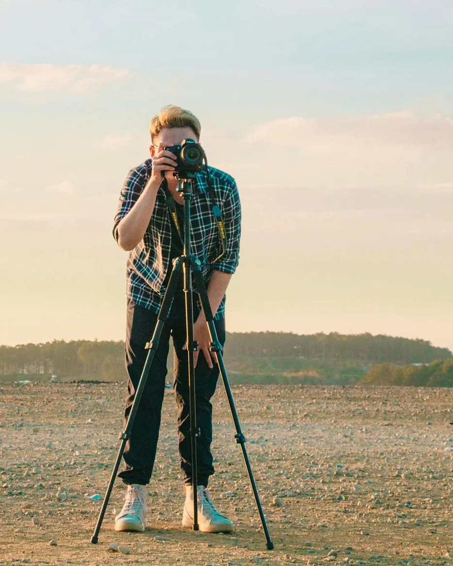 Person using a camera on a tripod outdoors at sunset.