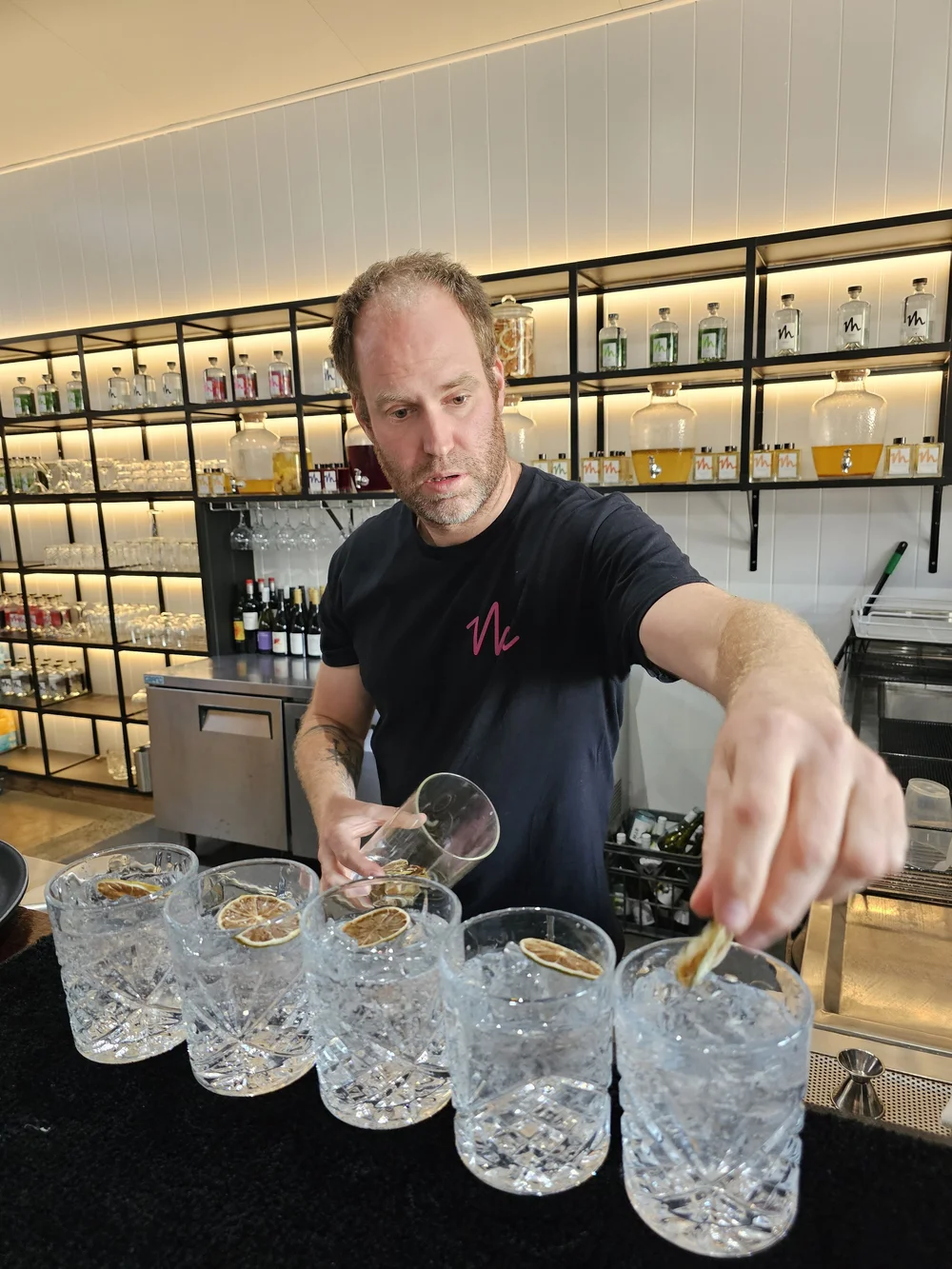 A distiller pouring tasting glasses behind the bar during a hens party gin class