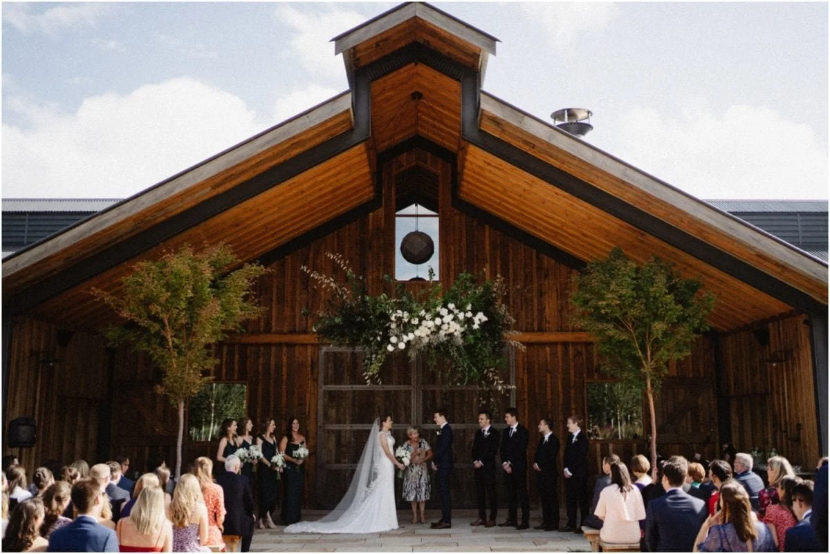 A wedding ceremony under the timber gable of a Southern Highlands barn venue, guests seated on both sides of the aisle