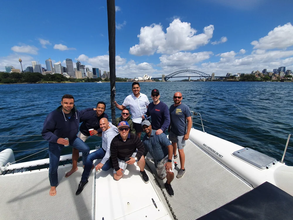 Group of mates on a catamaran on Sydney Harbour with the Opera House and Harbour Bridge behind them