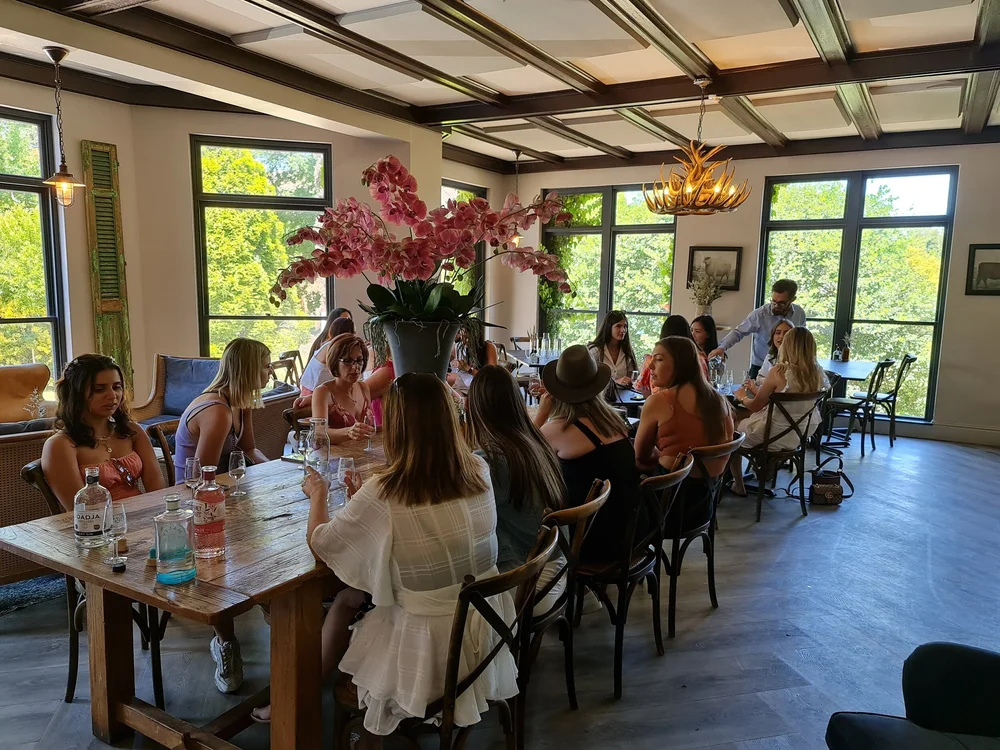 Fifteen guests seated along a long table set with gin bottles and glassware in a Southern Highlands dining room.