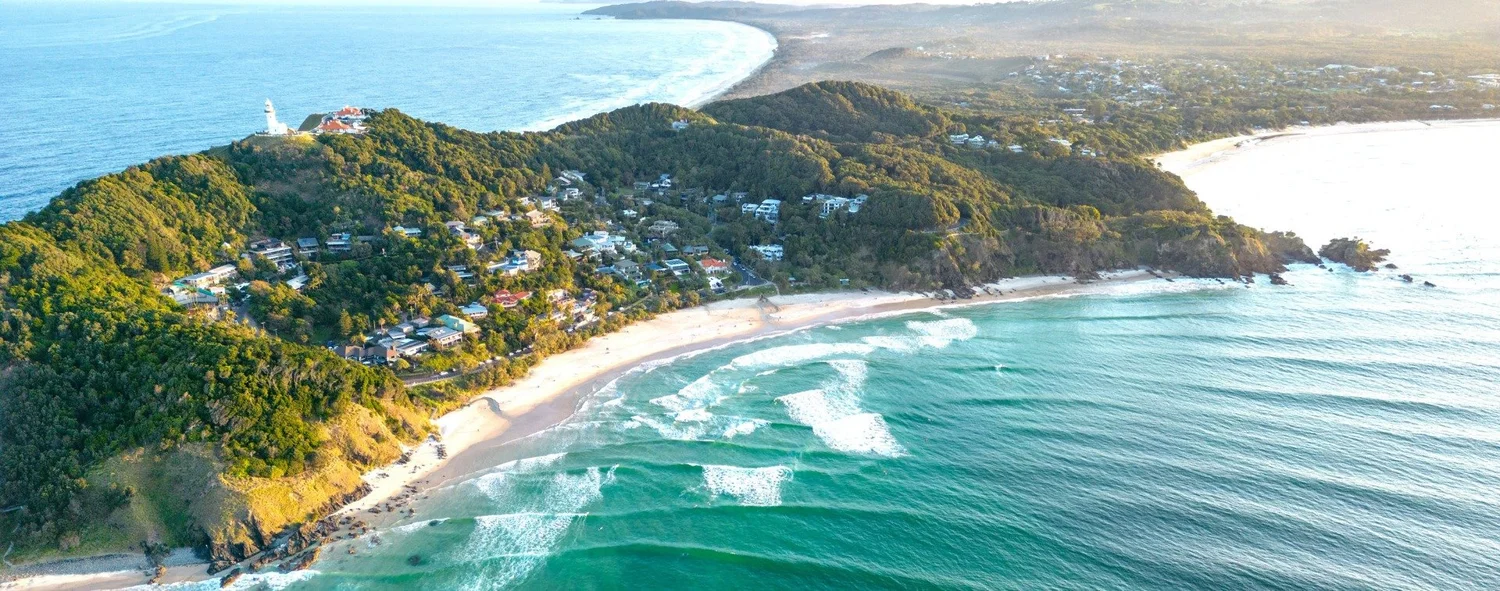 Aerial view of the Byron Bay coastline with the beach curving around towards the lighthouse headland