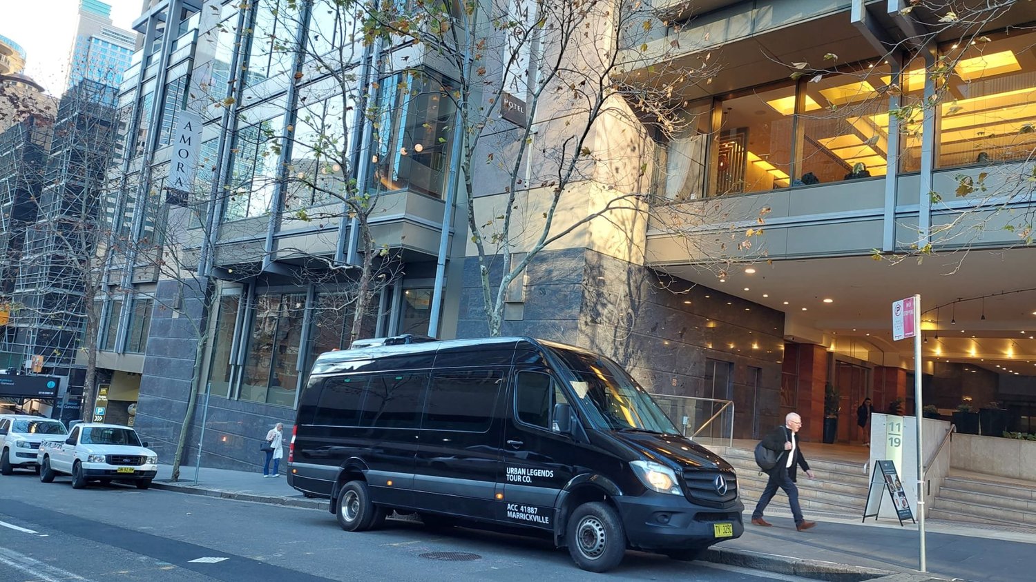 An 18-seat Mercedes Sprinter picking up guests outside a Sydney CBD hotel for an airport transfer.