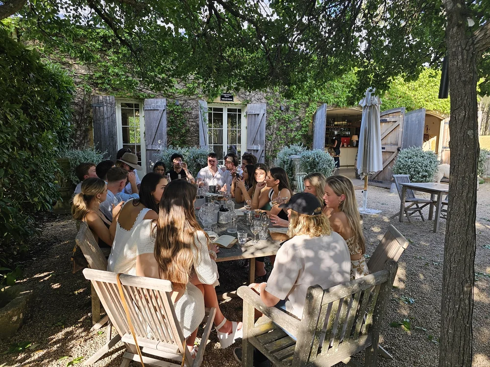 Corporate wine tour long lunch at a Southern Highlands cellar door Sixteen guests seated along a long outdoor table under trees at a rustic Southern Highlands cellar door.