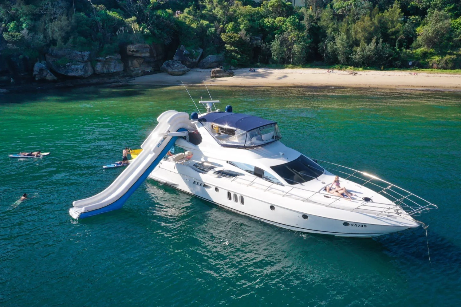 MV Maddison, a 62ft luxury motor cruiser, at anchor off a Sydney Harbour beach with its water slide out and guests on paddleboards
