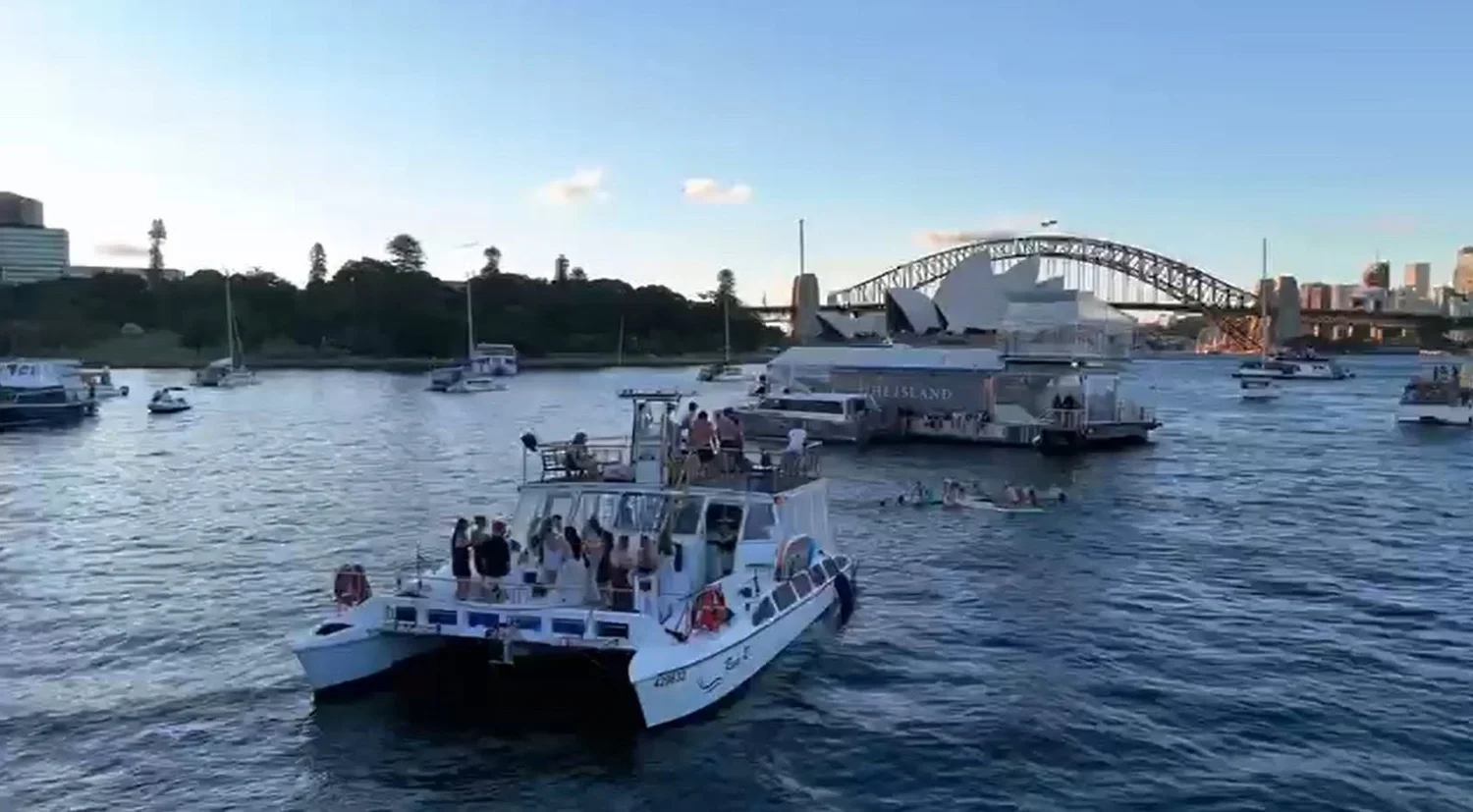 Rum Runner catamaran under way on Sydney Harbour with the Harbour Bridge and the city skyline behind