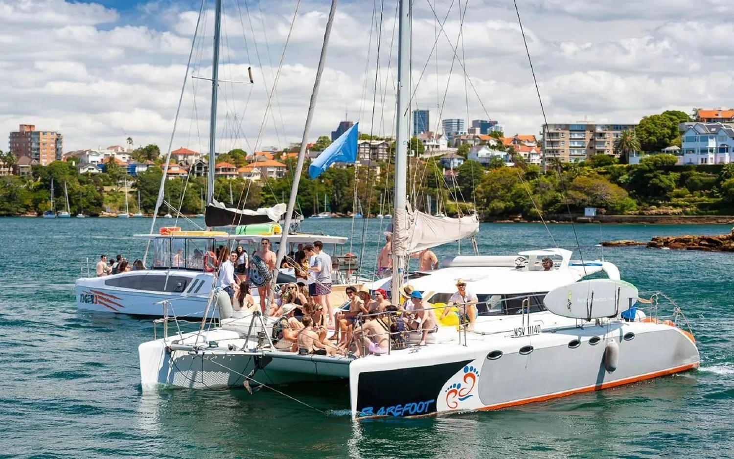 Barefoot, a 40ft sailing catamaran, cruising Sydney Harbour with a group on deck during a private charter