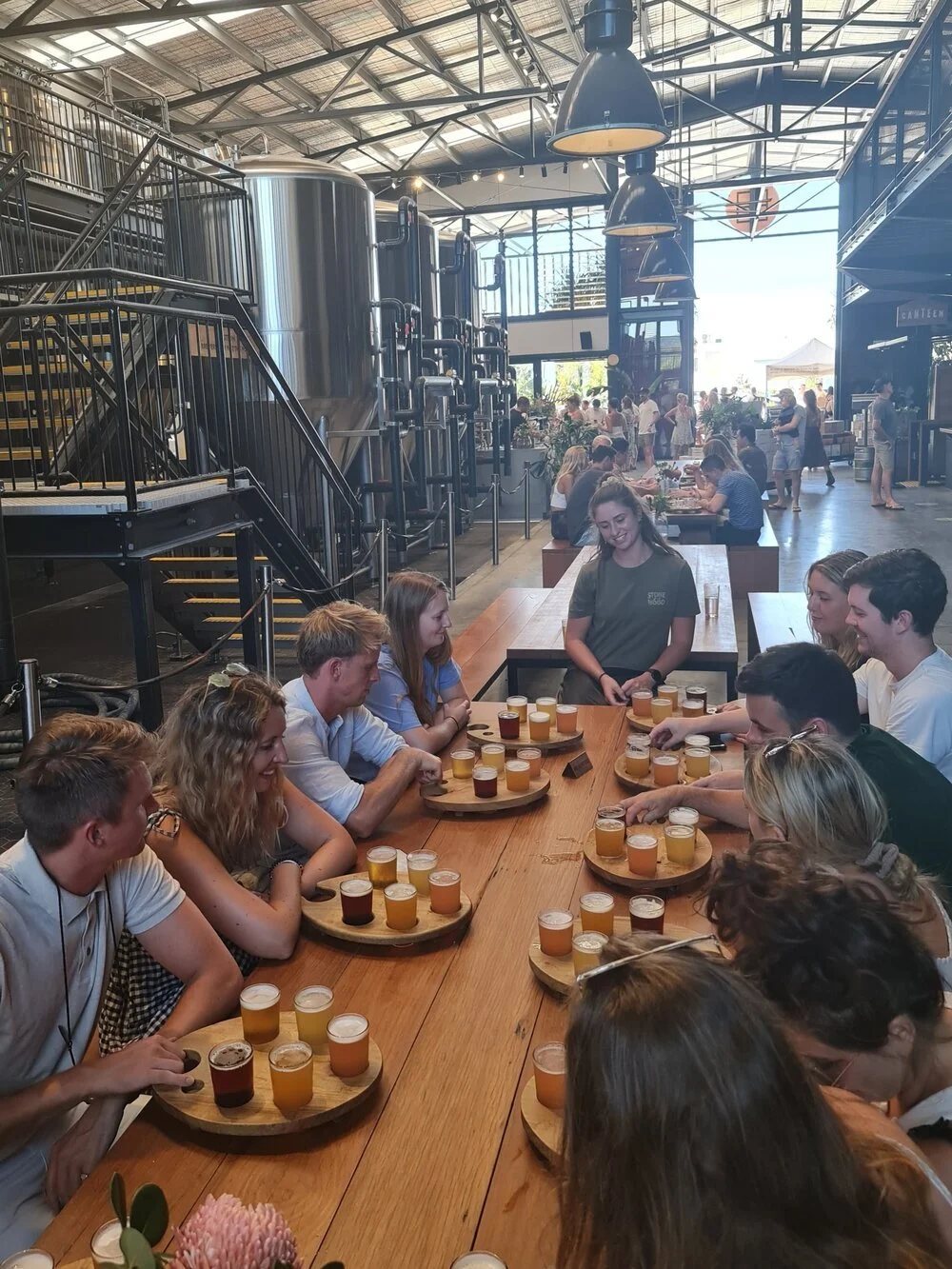 Private group sharing craft beer tasting paddles beside brewery tanks