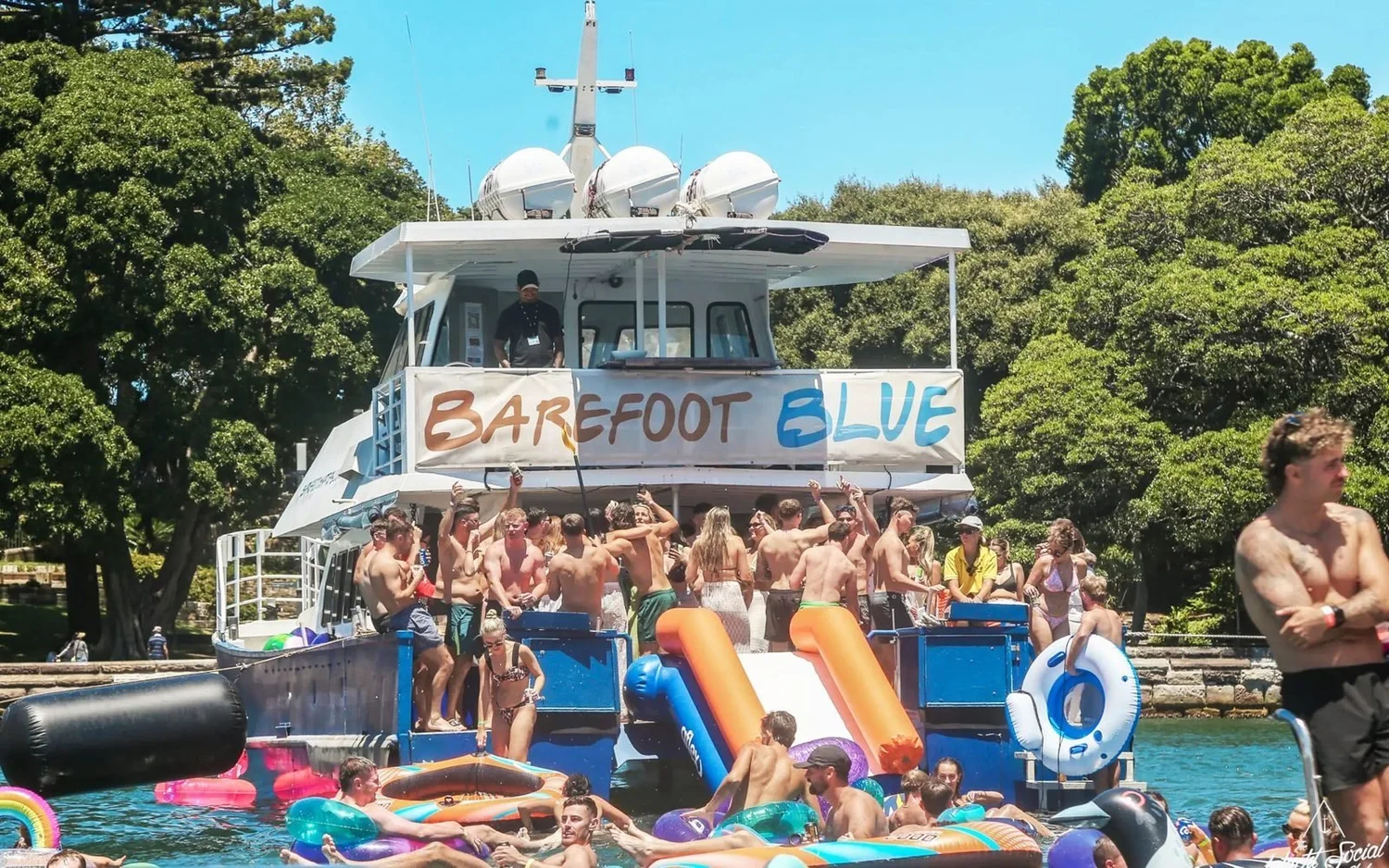 Barefoot Blue power catamaran at anchor on Sydney Harbour with a waterslide off the stern and a party group on deck