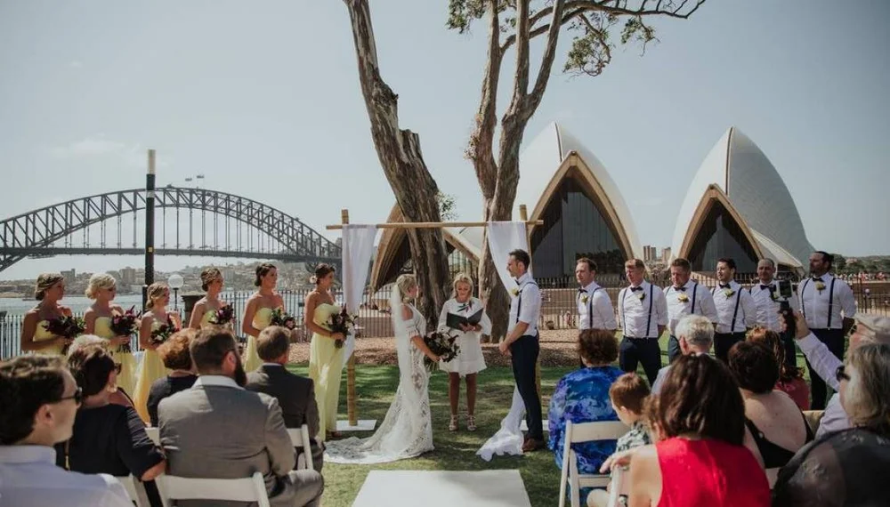 Wedding guests seated under an arbour at a Sydney harbourside ceremony, reached by private coach.