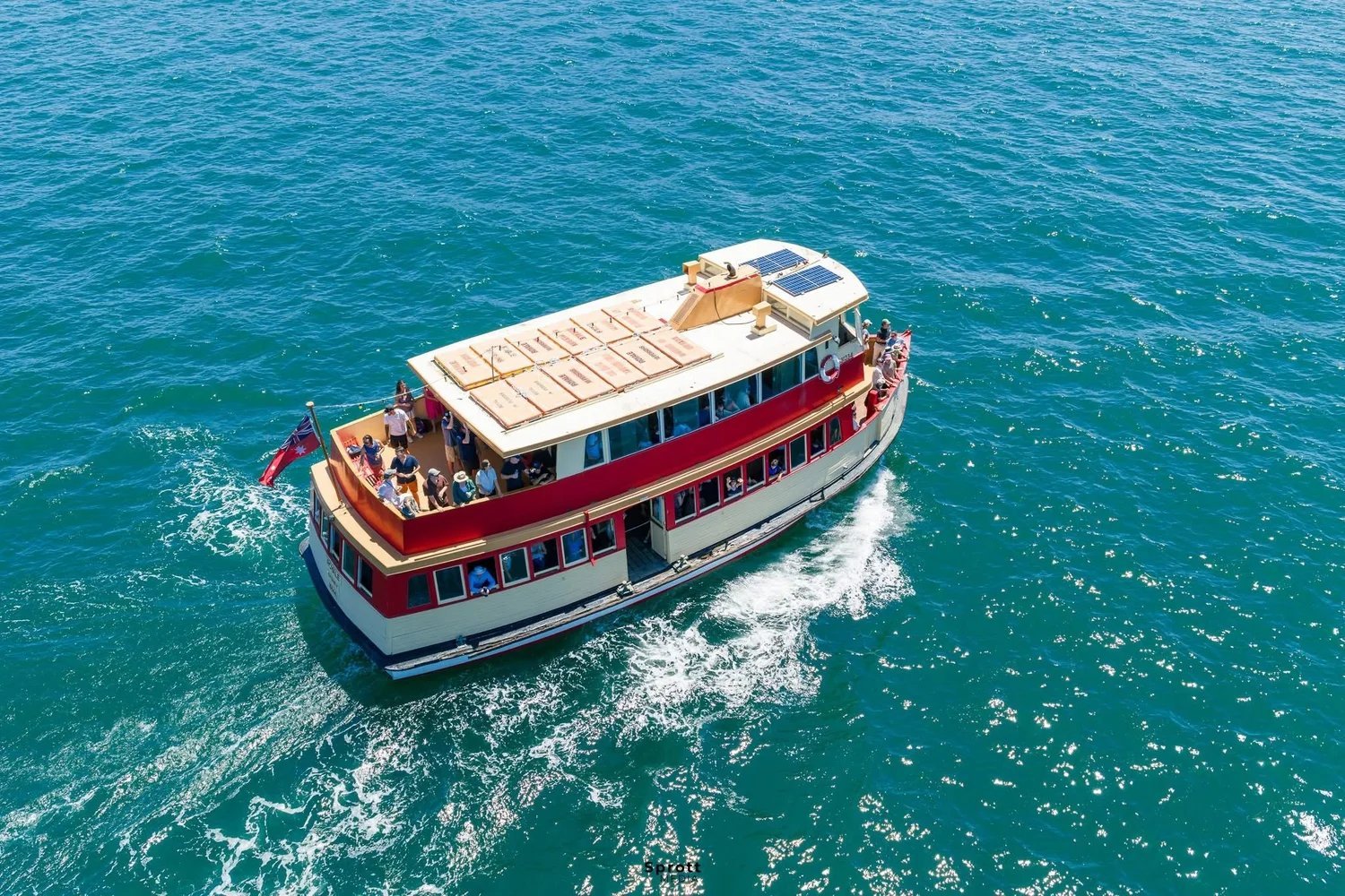 Aerial view of Royale, a red and cream heritage timber ferry, cruising on Sydney Harbour with guests on the top deck