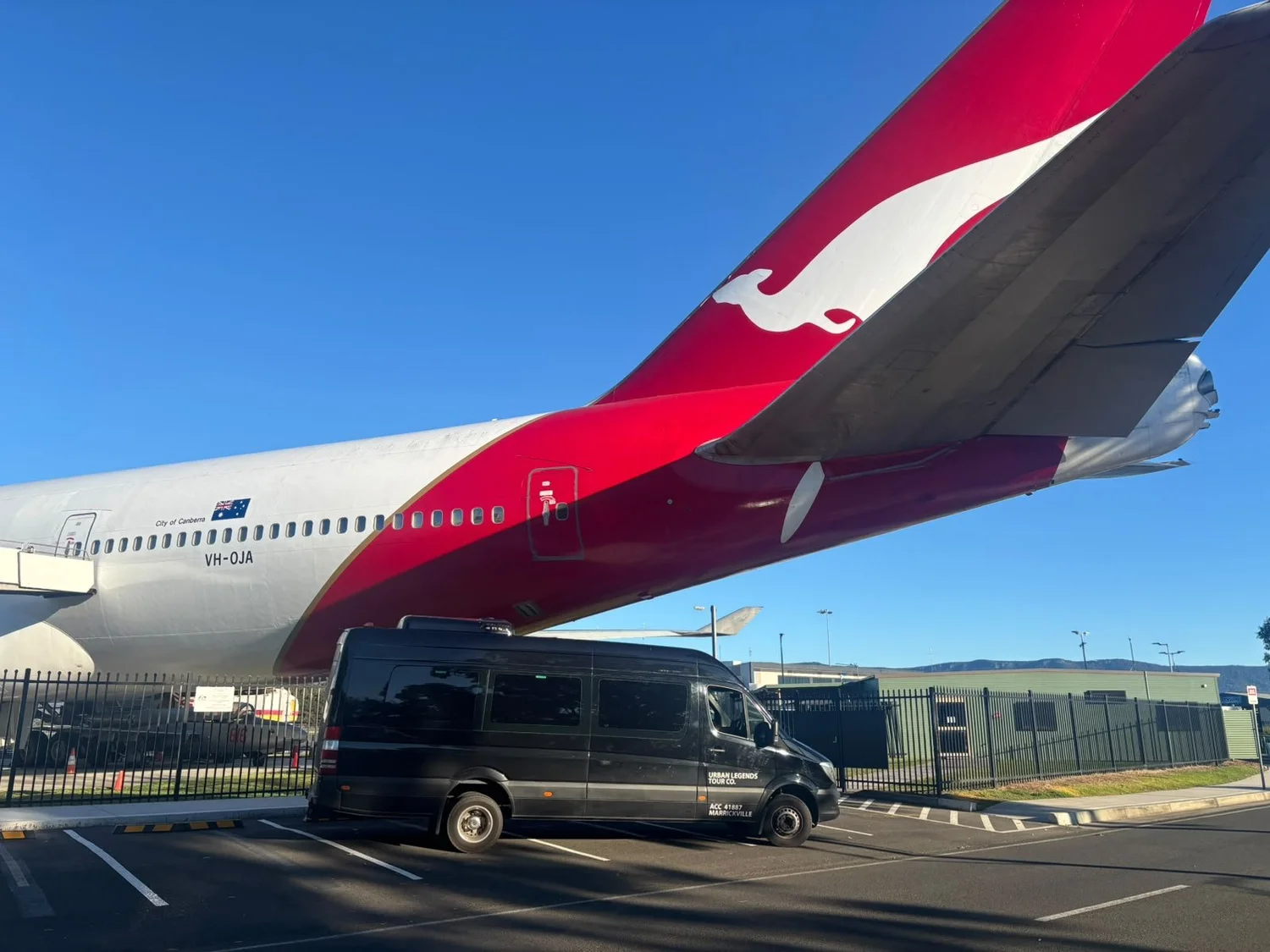 Urban Legends black Mercedes Sprinter parked beneath the tail of a Qantas Boeing 747 at HARS Aviation Museum, Albion Park