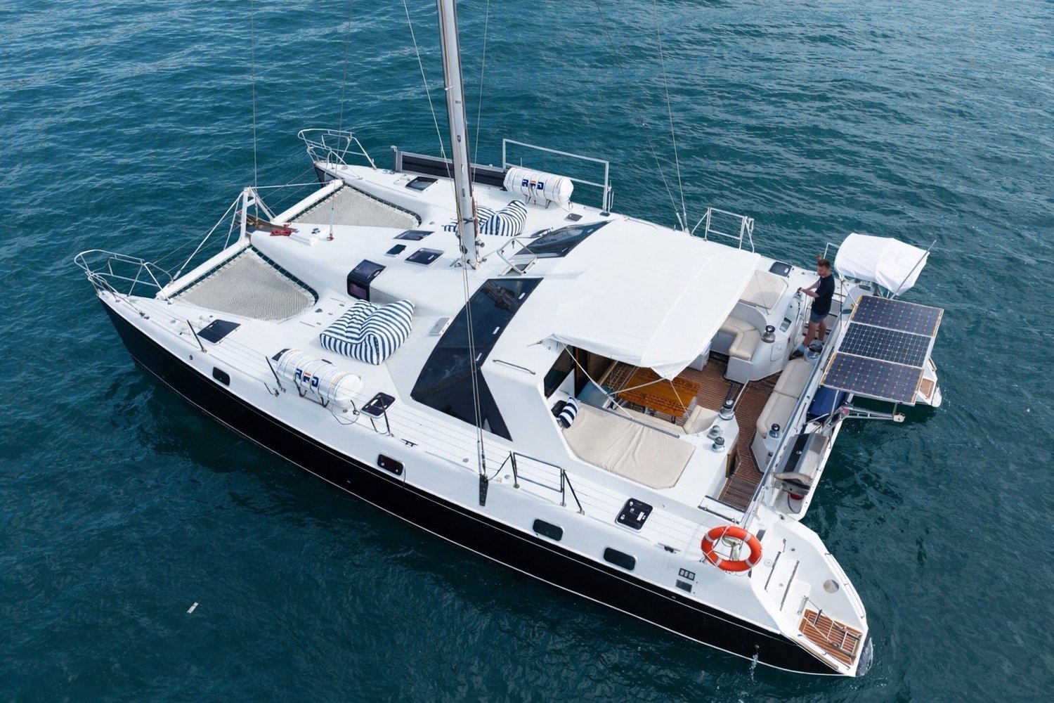 Aerial view of the Obsession sailing catamaran at anchor on Sydney Harbour, white hull with black trim, front trampolines and a shaded cockpit
