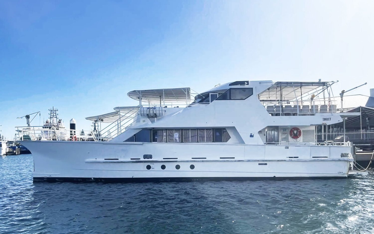 Barefoot Spirit, a 20m power catamaran with covered upper decks, berthed at a wharf on a clear blue day, seen side on