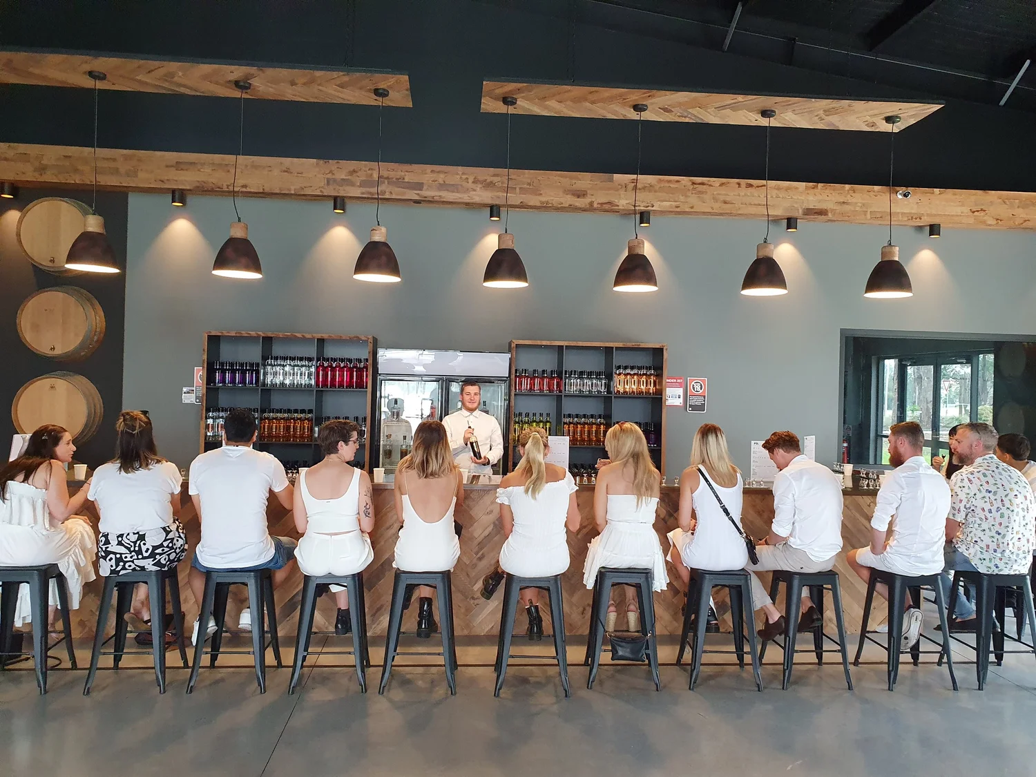 Guests seated along a distillery tasting bar in the Hunter Valley with pendant lights overhead and spirit bottles on the back shelves, on a half day brewery tour.