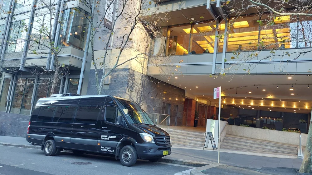 A black Urban Legends Mercedes minibus waiting at the entrance of a Sydney hotel