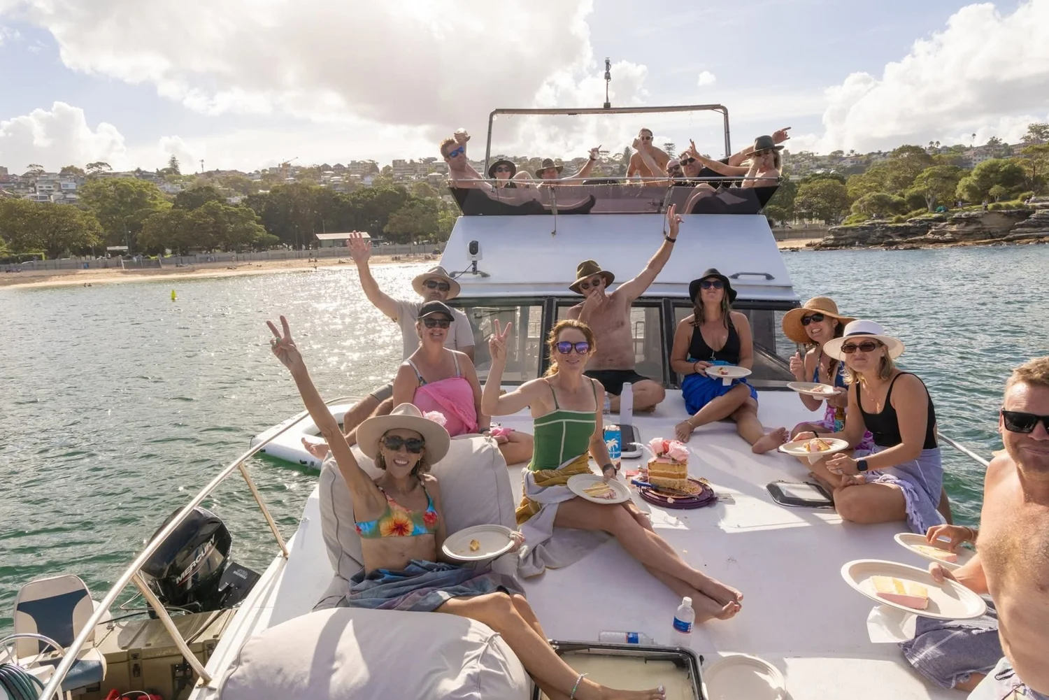 A birthday group in sun hats celebrating on the bow and flybridge of Mayfair at anchor in a Sydney Harbour bay